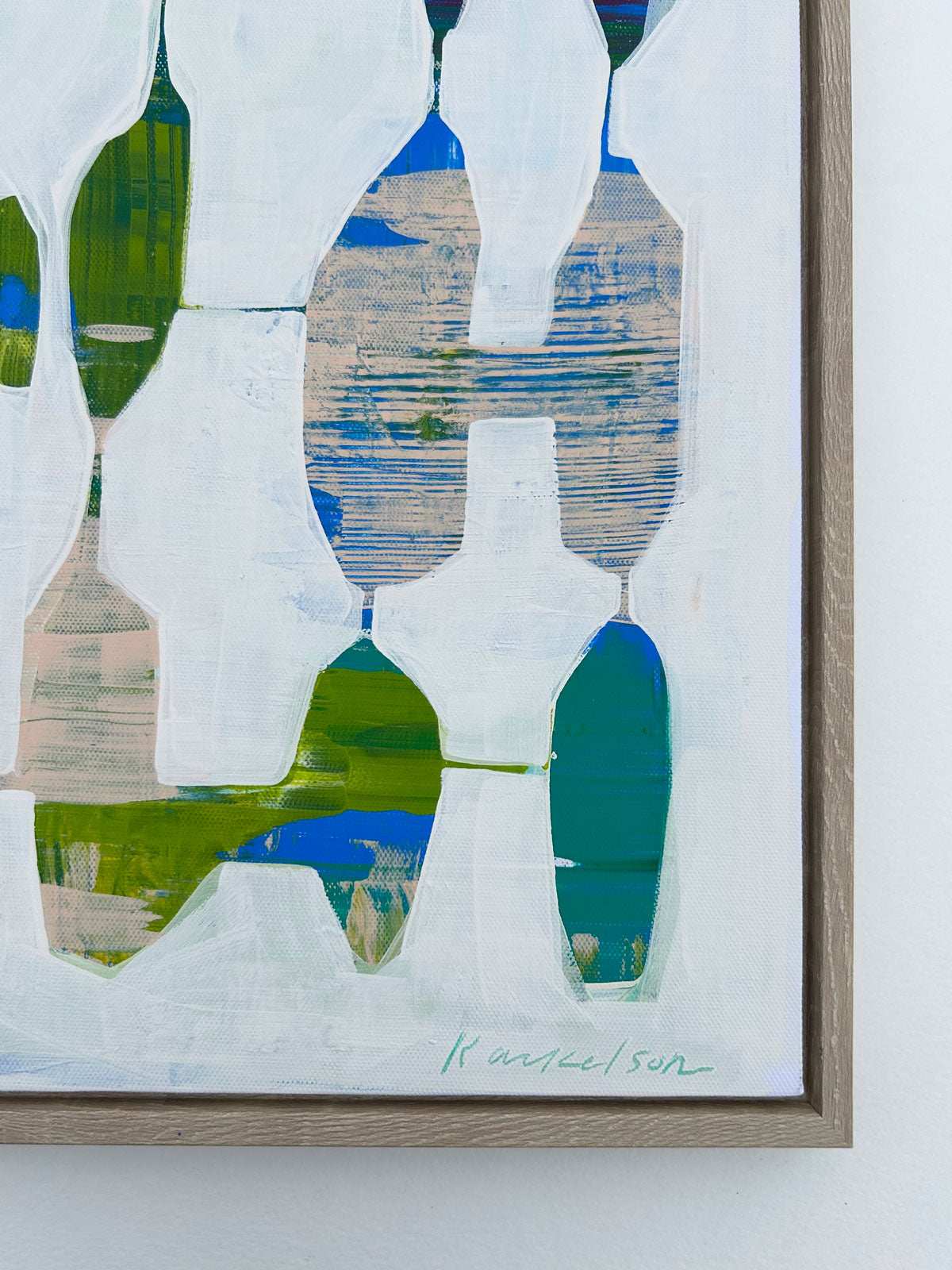 A detail of a framed abstract painting hangs on a white wall. 