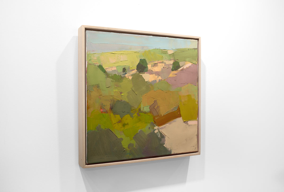 A green abstracted landscape painting framed in a wood floating frame hangs on a white wall.