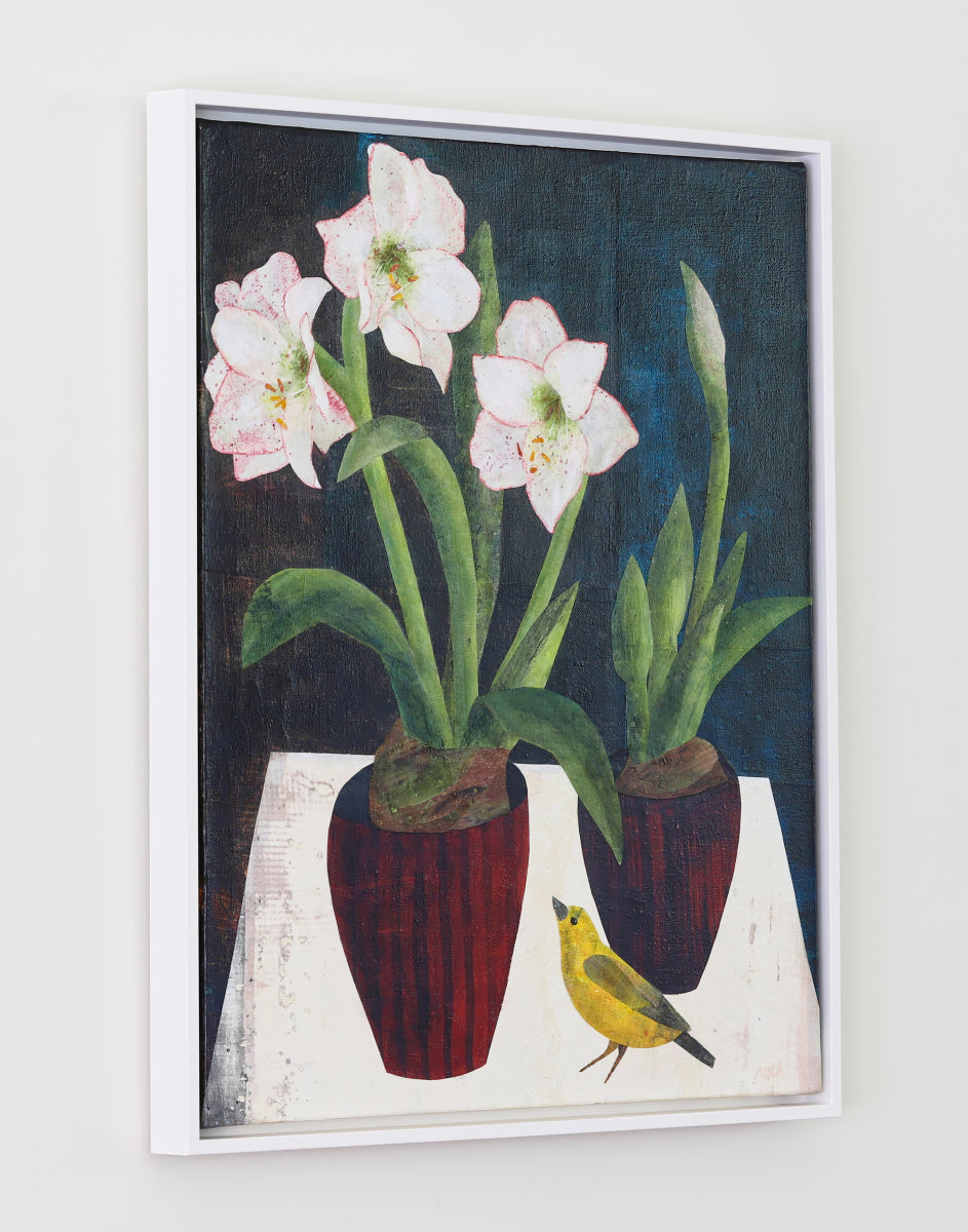 A framed still life painting featuring two potted white flowers with green stems and leaves, a small yellow bird, and a dark blue background, displayed on a light wall.