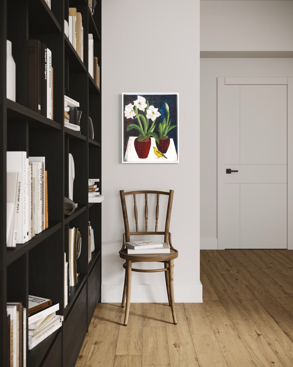 A floral collage painting hangs on a white wall above a wooden chair next to a black built in bookshelf. 