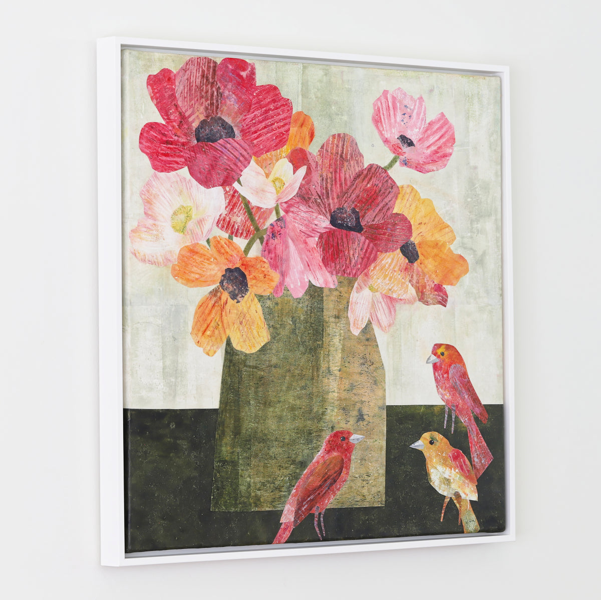 A framed collage featuring a still-life floral scene with large pink, red, and orange flowers in a vase, plus three small birds, shown hanging on a light gray wall.