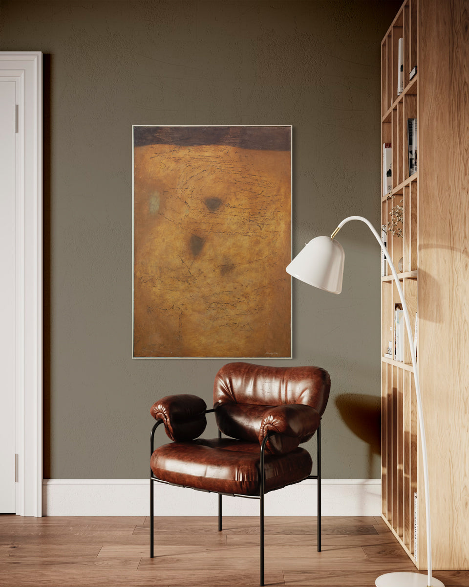 A warm yellow and brown abstract painting hangs on a dark wall above a leather chair, white floor lamp, and next to a large wooden bookshelf. 