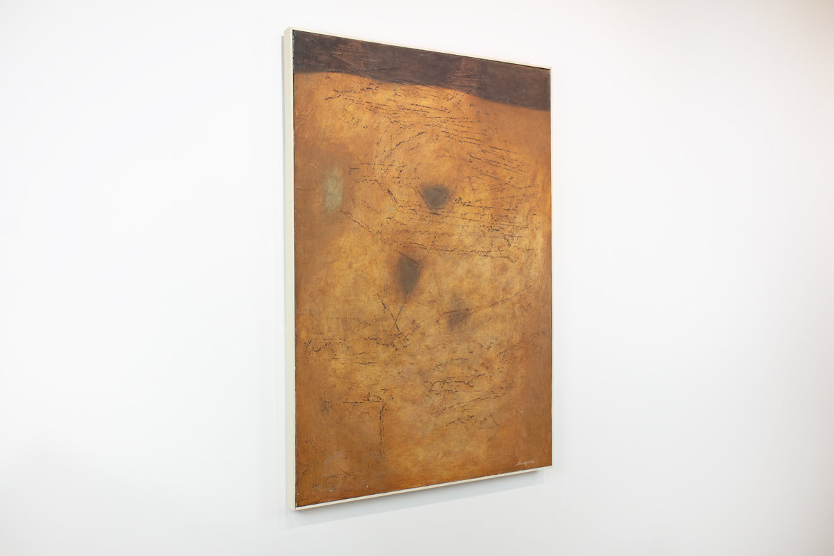 A warm yellow and brown abstract painting hangs on a white wall.