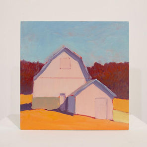 A painting of a pink barn in front of red trees sits upright on a white table surface in front of a white wall.