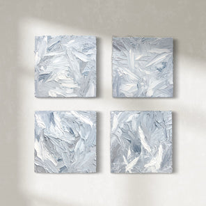 Four 12x12 inch paintings thickly painted with palette knife strokes in blue, white and grey hang on a wall.