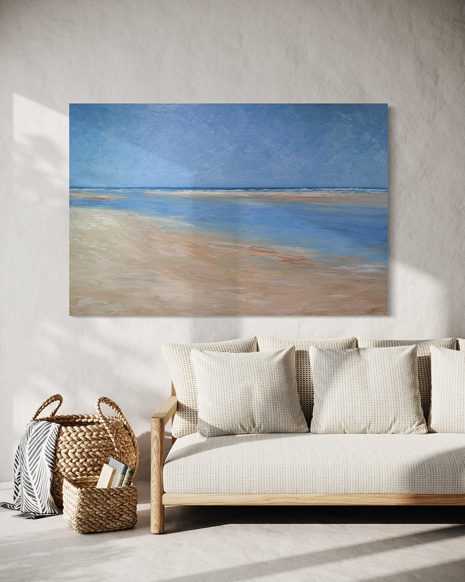 A textured blue and beige coastal painting of a beach hangs on a white wall above a light cream colored sofa with wicker baskets to the side. 