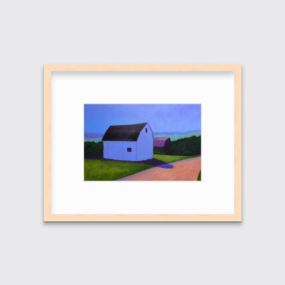 Fine art print of two barns, blue and purple, surrounded by green grass, a rose colored road and a blue sky in a natural wood frame with a mat hangs on a white wall.