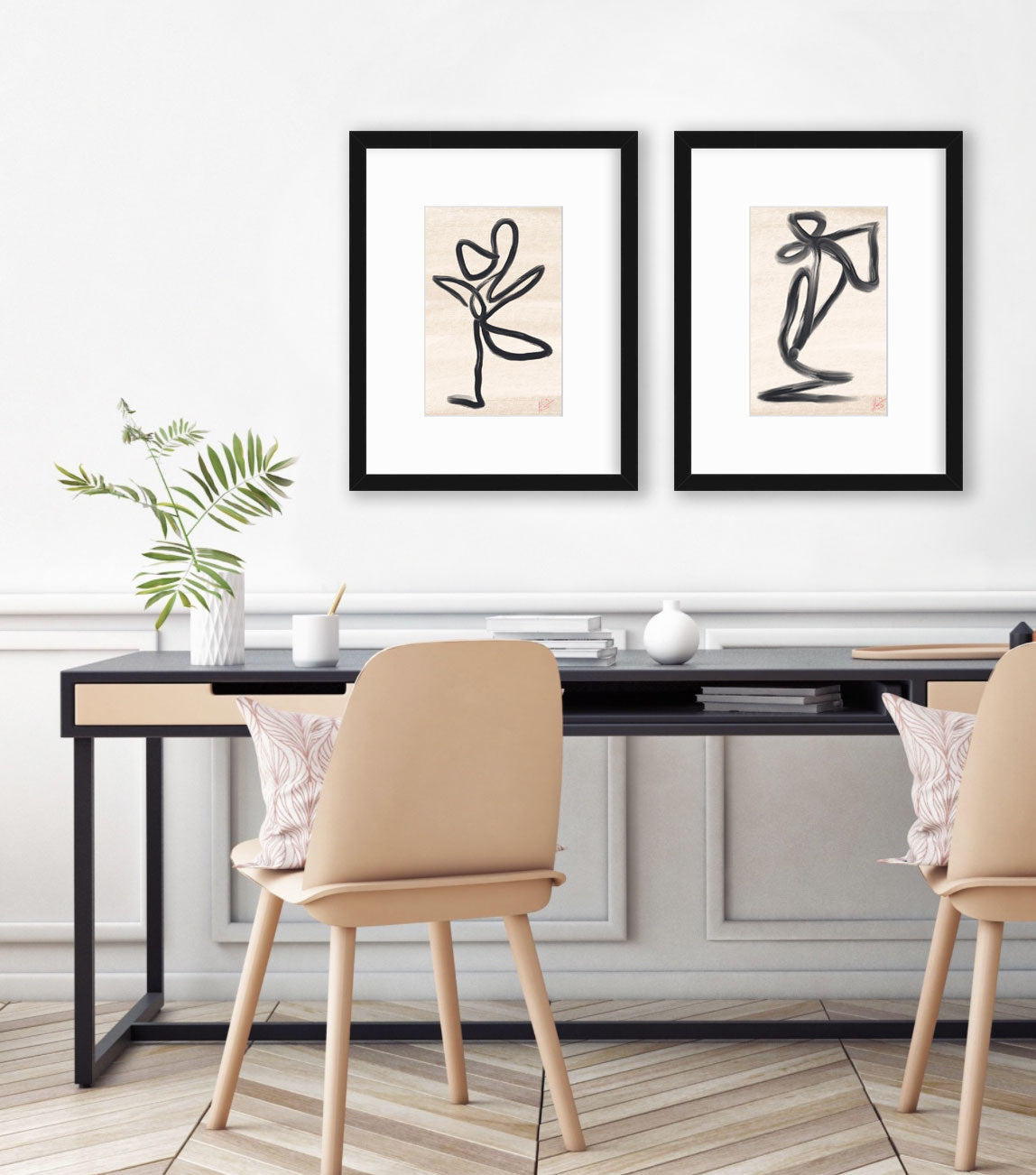 Two black minimalistic art prints hang on a white wall above a modern black desk and wooden chairs. 