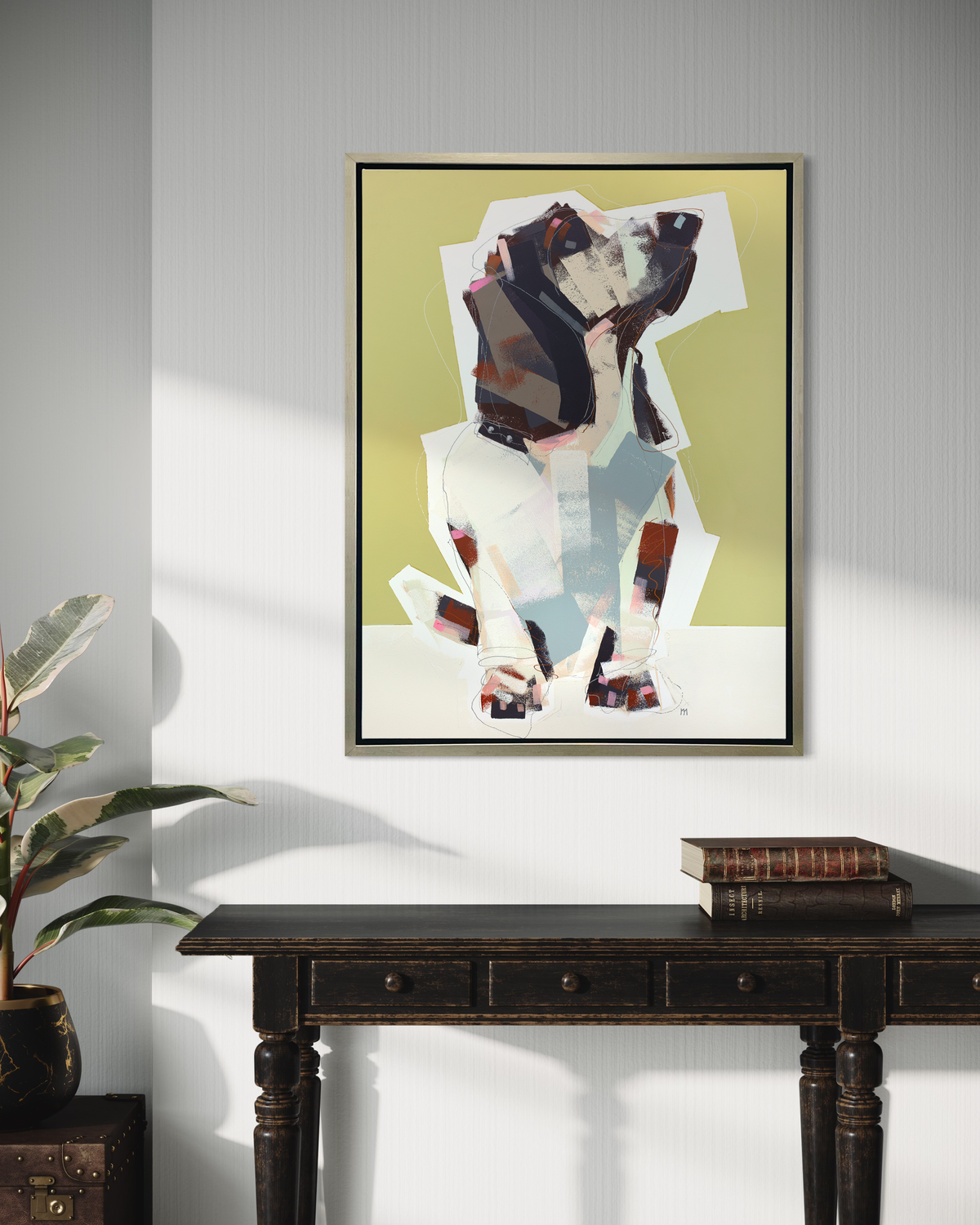 A chartreuse, navy, beige and light blue abstract dog print in a silver floater frame hangs on a white wall above a dark stained wood console table with two books.