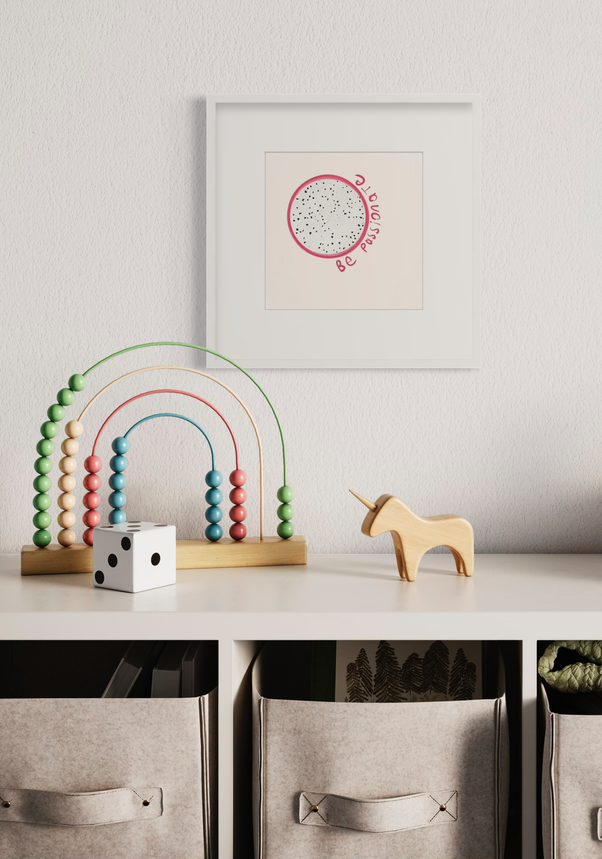 An art print of a minimalistic abstract fruit with the words "be passionate" in a white frame with a mat hangs on a white wall above a white storage shelf with a multicolored rainbow toy, a small wood unicorn figurine and a white and black die.