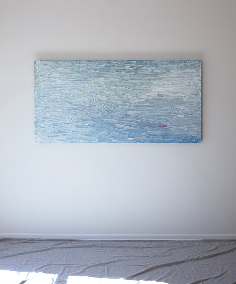 A abstract painting with blue textured brushstrokes is seen hanging on na wall at the artists studio.