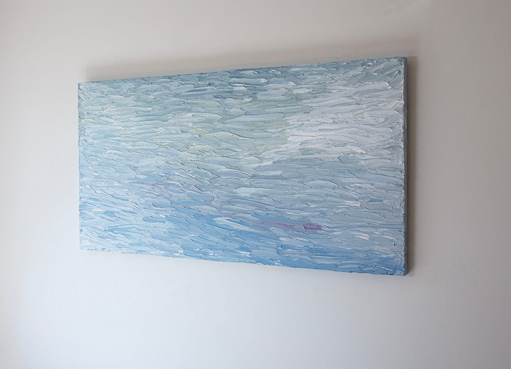 A abstract painting with blue textured brushstrokes is seen at an angle on a gallery wall.