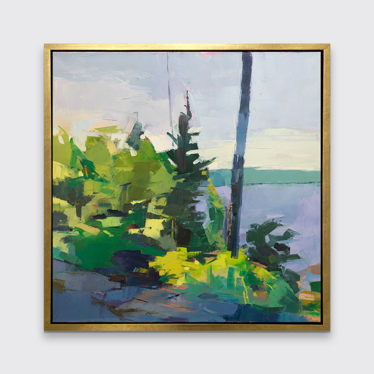 An abstract blue and green landscape print framed in a gold frame hangs on a white wall.