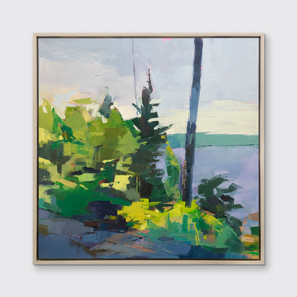 An abstract blue and green landscape print framed in a white oak frame hangs on a white wall.