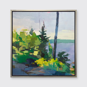 An abstract blue and green landscape print framed in a silver frame hangs on a white wall. 