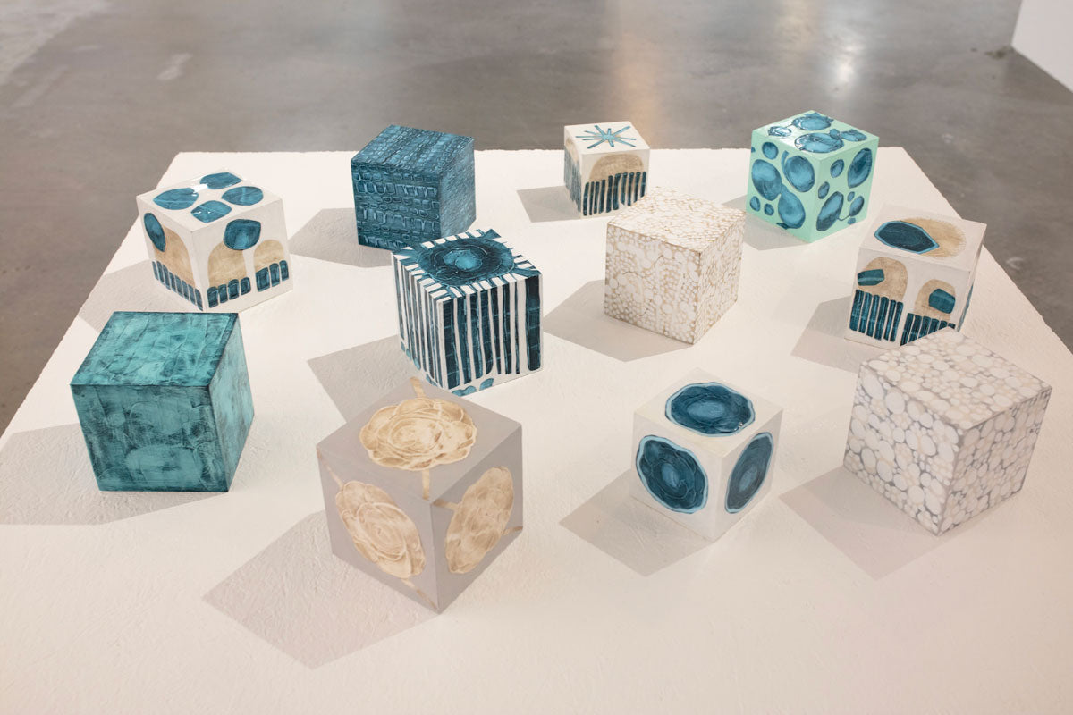 A collection of blue, white, and beige painted cubes rest on a white surface. 