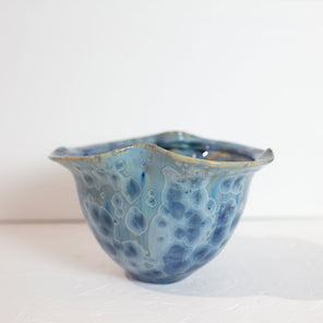 A blue glazed ceramic bowl rests on a white surface in front of a white wall.
