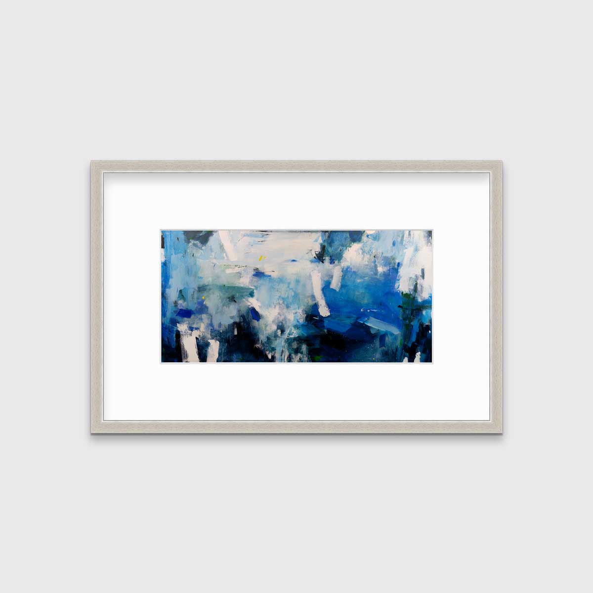 A blue and white abstract print in a silver frame with a mat hangs on a white wall.
