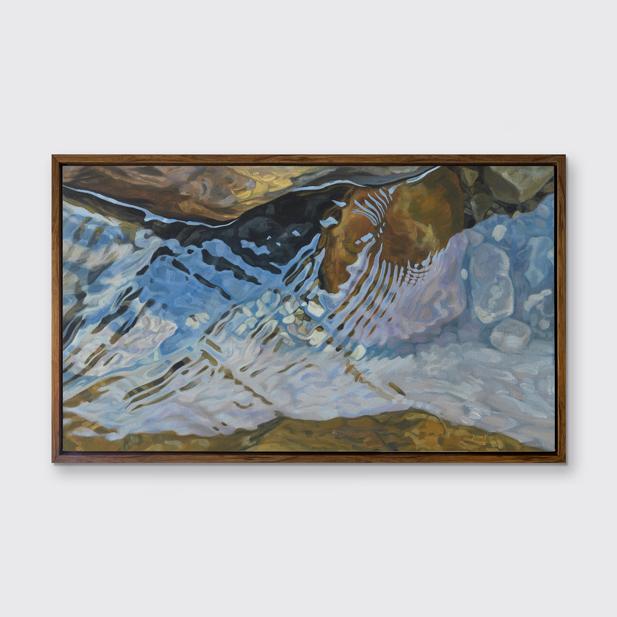 A print of water reflecting over river rocks framed in a wood frame hangs on a white wall.