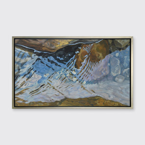 A print of water reflecting over river rocks framed in a warm silver frame hangs on a white wall. 