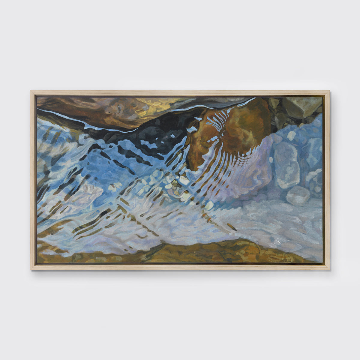 A print of water reflecting over river rocks framed in a light wood frame hangs on a white wall.