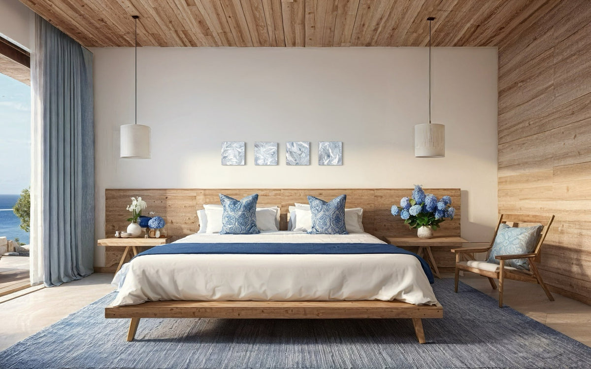 Four 12x12 inch paintings thickly painted with palette knife strokes in blue, white and grey hang on a wall over a bed in horizontal display.
