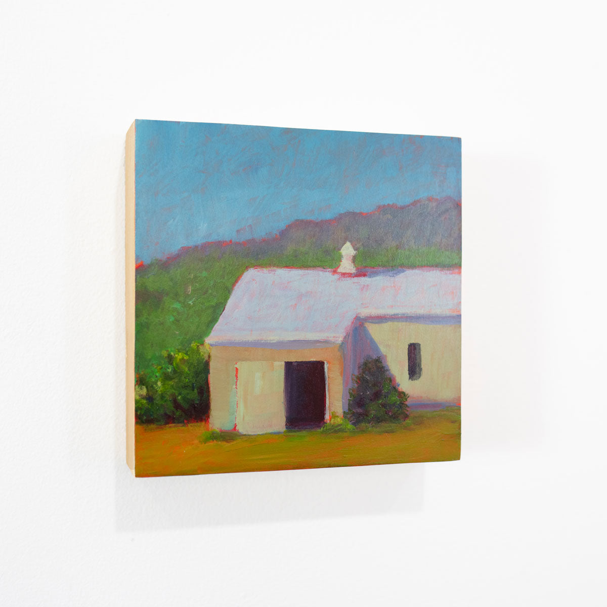 A small blue, green, and yellow landscape painting hangs on a white wall.
