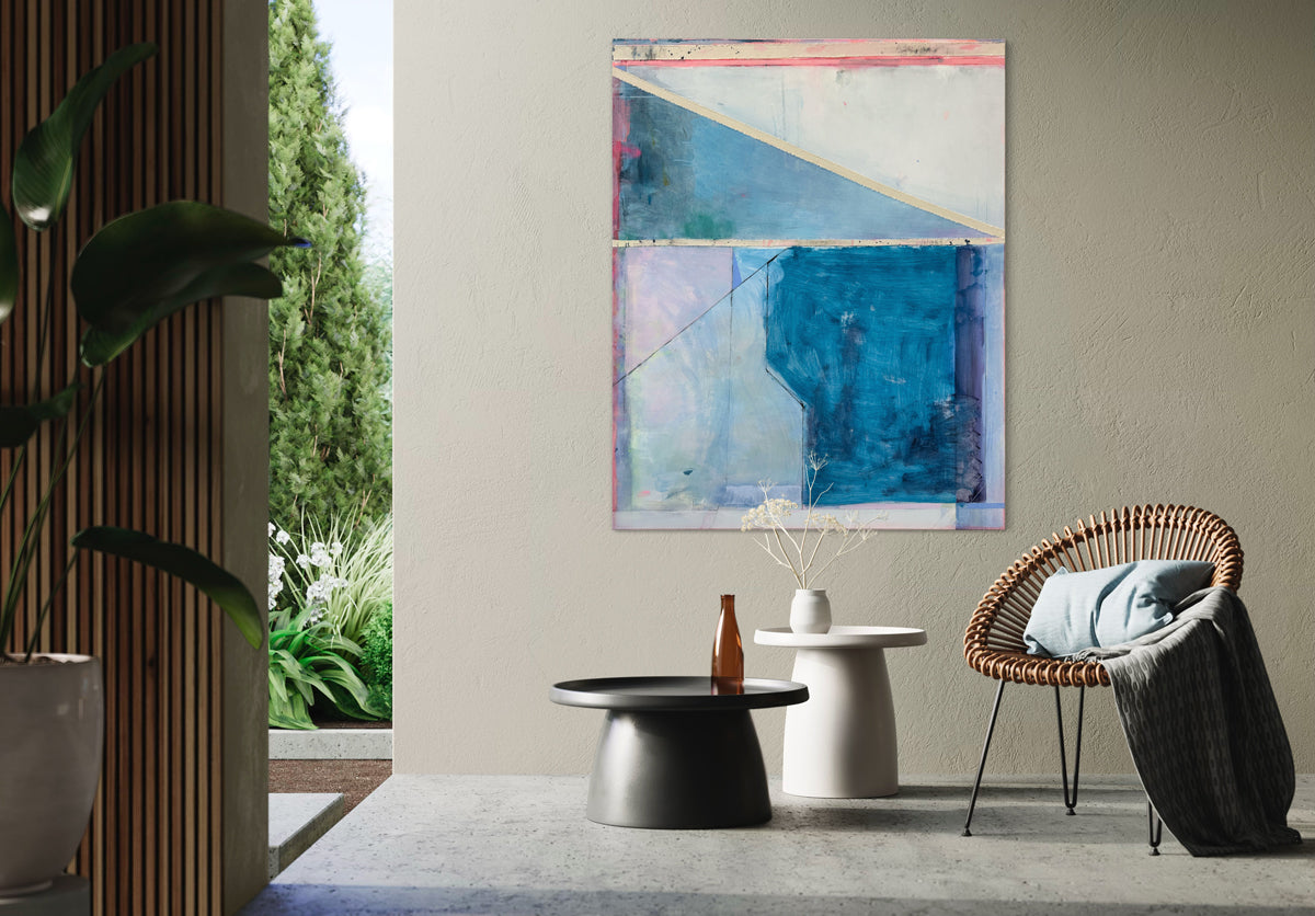 A blue and pink geometric abstract painting hangs on a beige wall above a rounded chair with a throw blanket and two coffee tables with decorative accents.