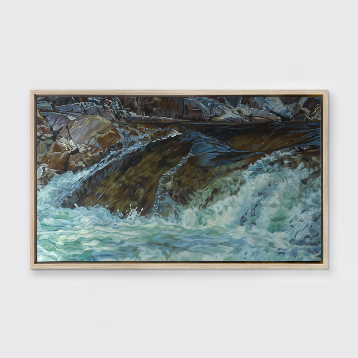 A print of river water streaming over rocks framed in a light wood frame hangs on a white wall.