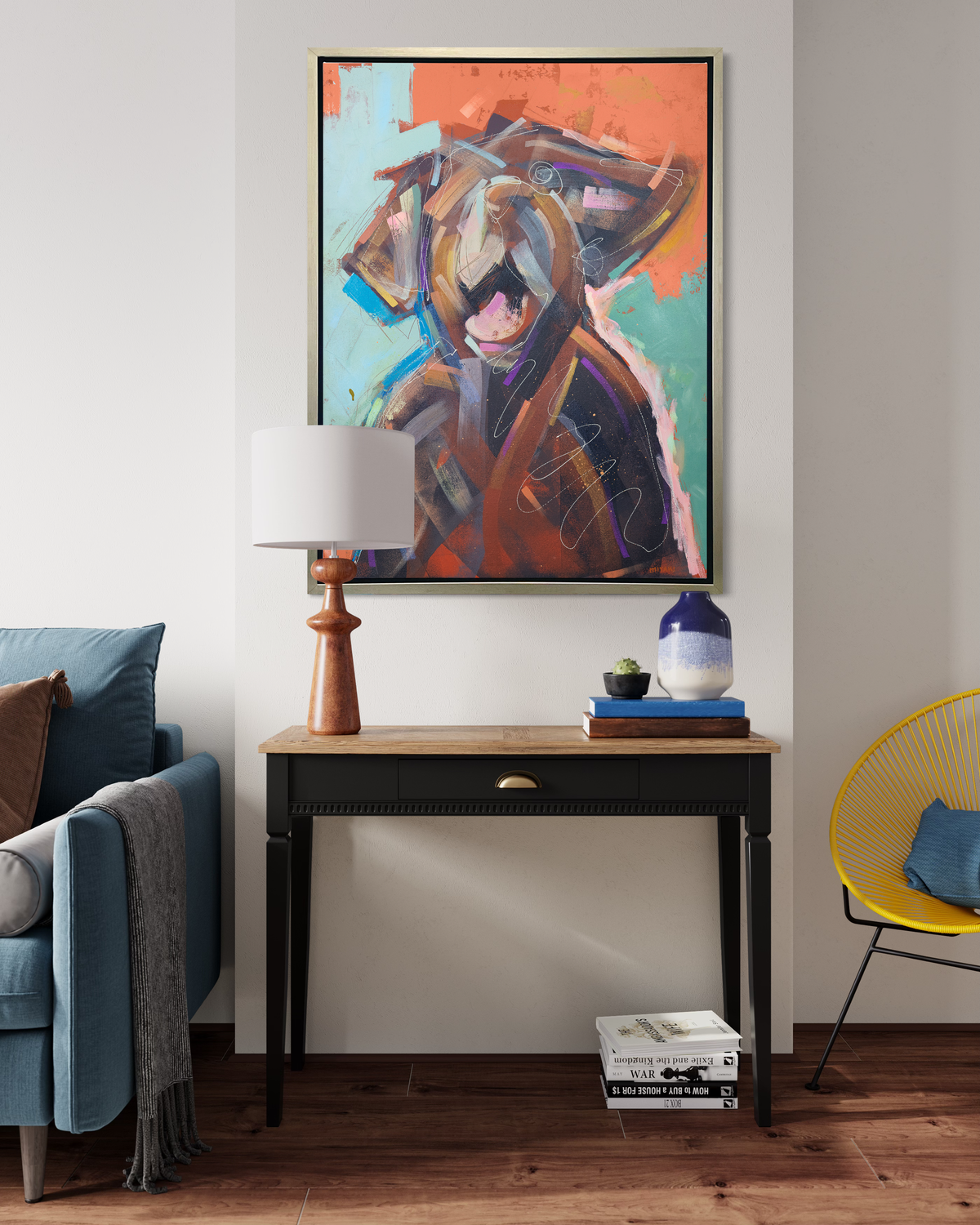 A orange, brown, teal and light pink abstract dog print in a silver floater frame hangs on a white wall above a wood and black console table with a table lamp and a stack of books.