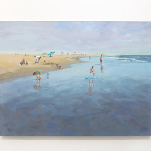 A light blue painting of people playing on a beach shoreline hangs on a white wall. 