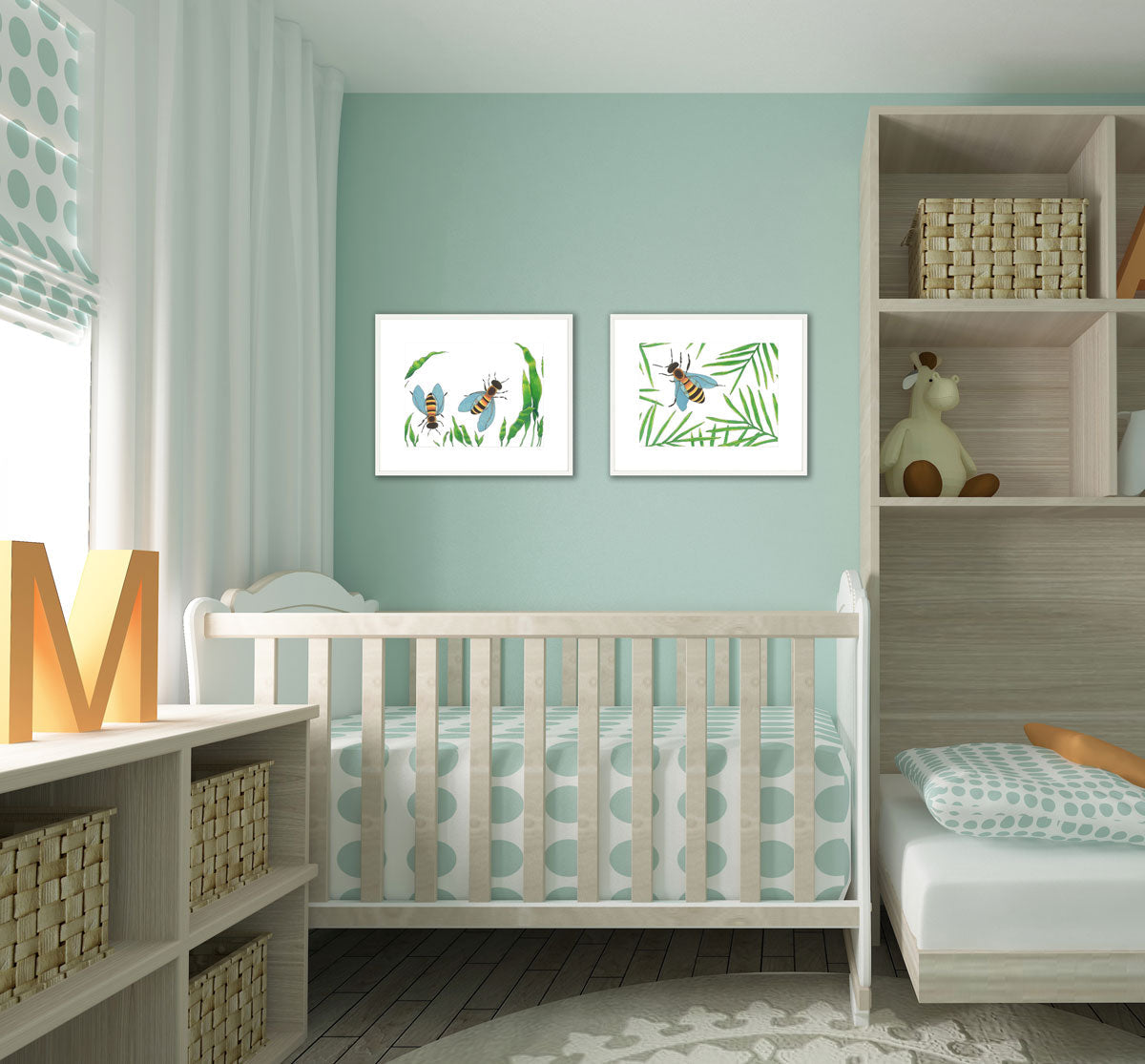 Two white and green bee illustration prints by Elizabeth Iadicicco in a white frame with a mat hangs on a light blue wall in a baby's room above a the light grey wood crib with polka dot bedding. 
