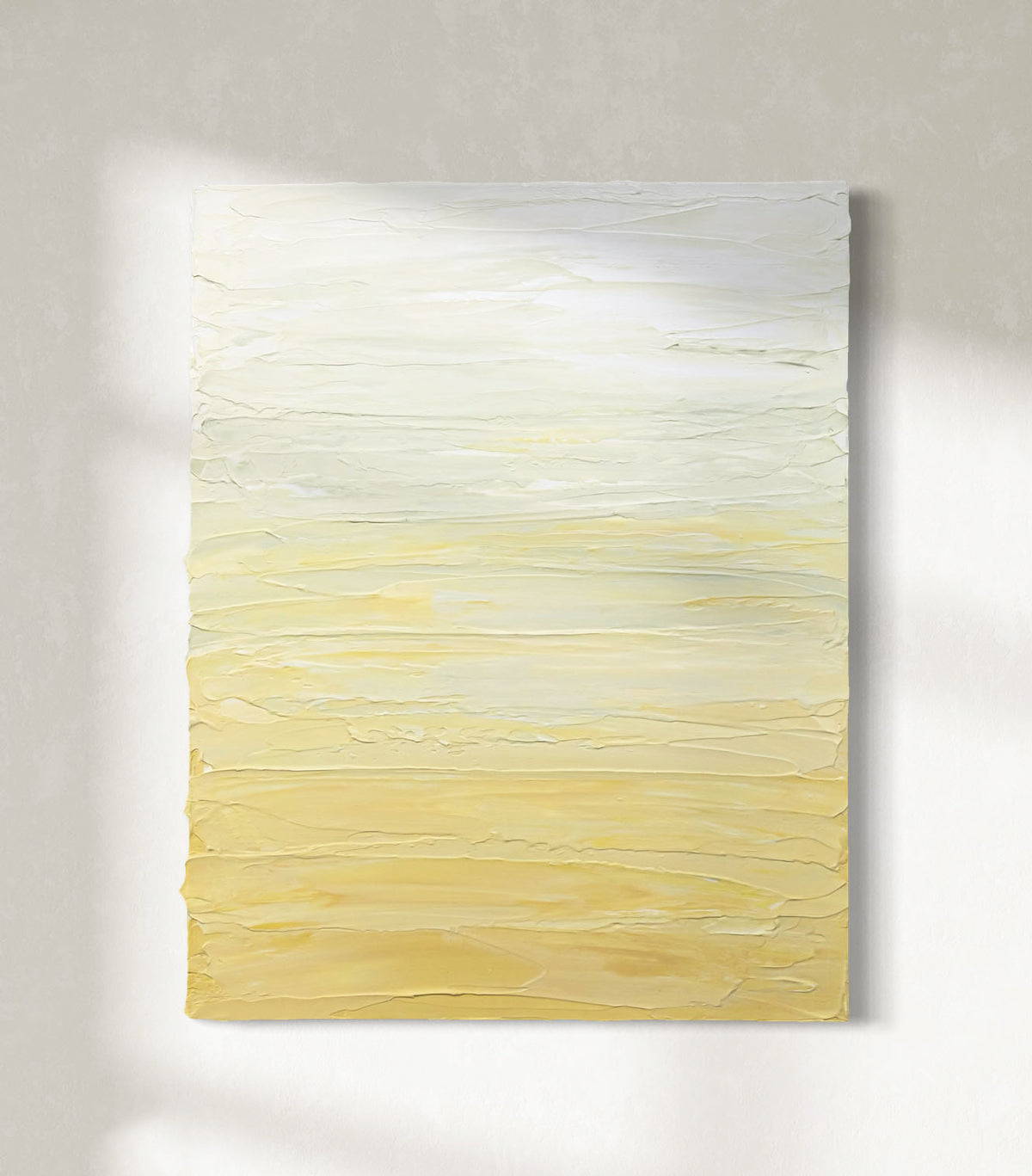 A Yellow, seafoam green and white textured painting by Teo Guererra hangs on a wall in the sunlight.