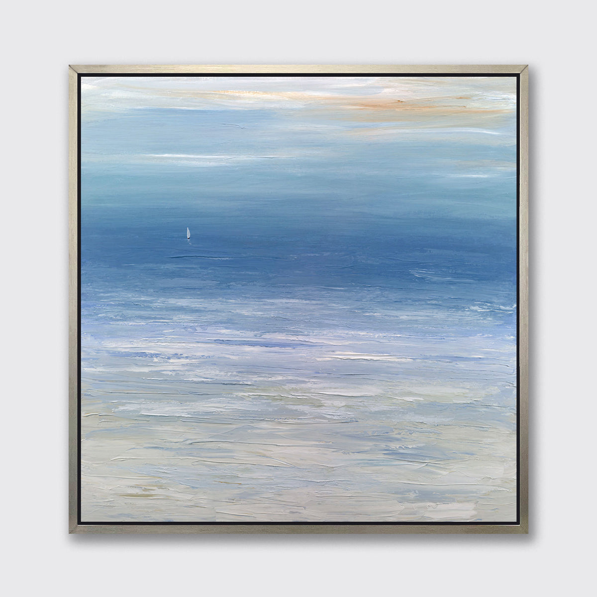 A blue, white and beige abstract seascape print in a silver floater frame hangs on a white wall.