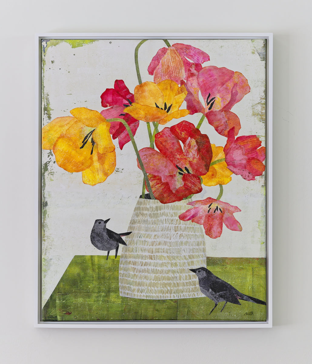 A framed collage featuring a bouquet of vibrant yellow, red, and pink tulips in a textured white vase, with two small black birds on a green surface against a distressed off-white background.