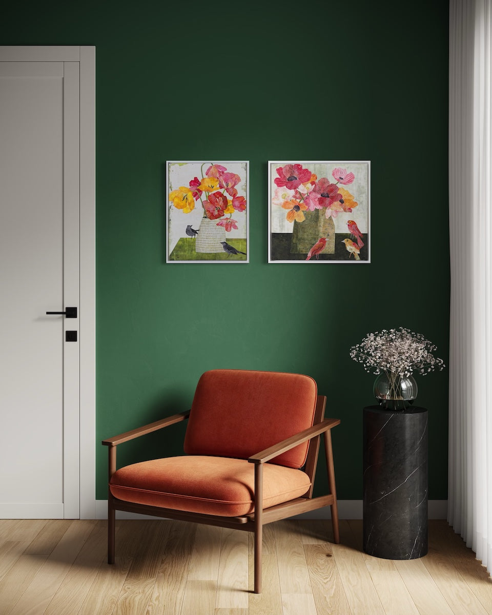 A styled interior scene with a dark green wall, two framed floral collage paintings, a rust-orange upholstered wooden armchair, a black marble side table, and a white door on the left.