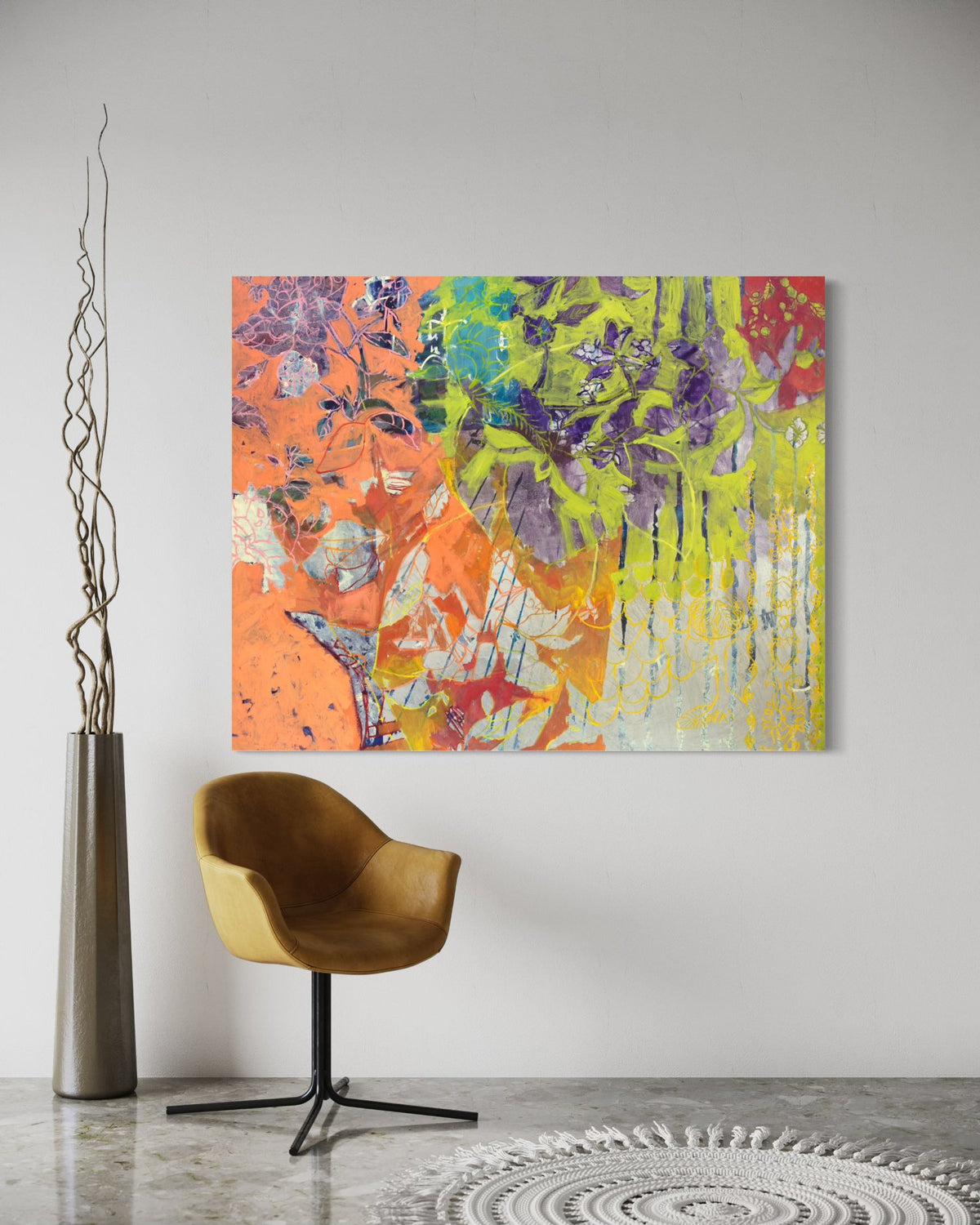 A painting with beautiful floral motifs in neon green, purple, orange, and blue is hung on a wall with a chair and tall silver vase holding decorative twigs sitting in front. The painting is wired and ready to hang.