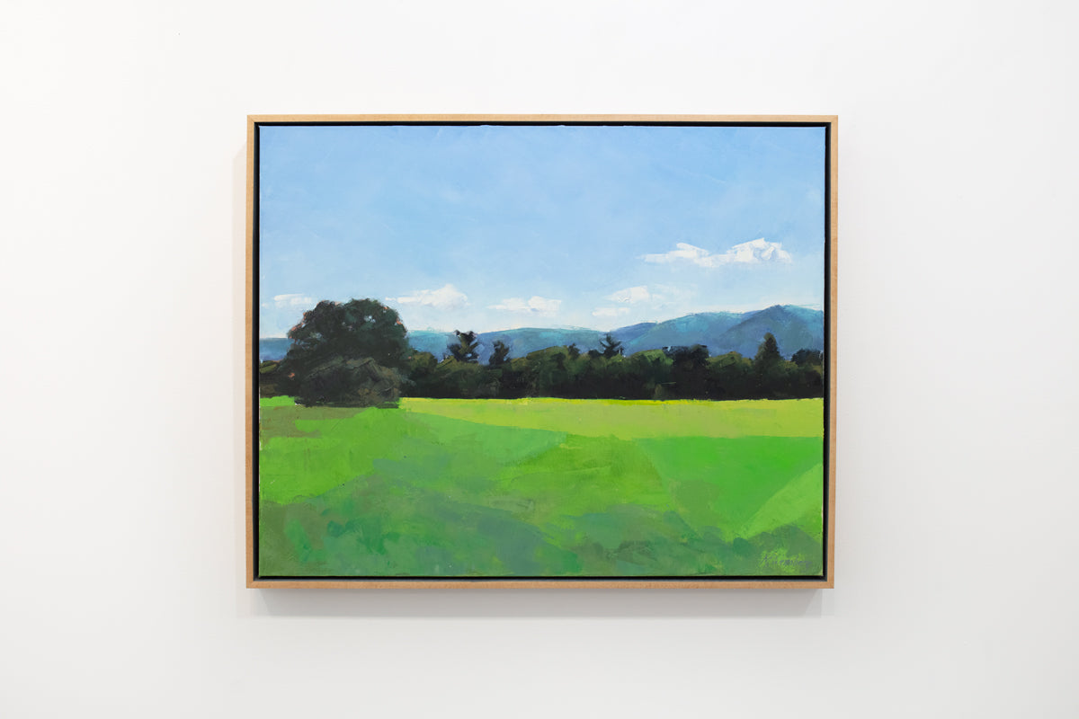 A blue and green landscape painting in a wood frame hangs on a white wall. 