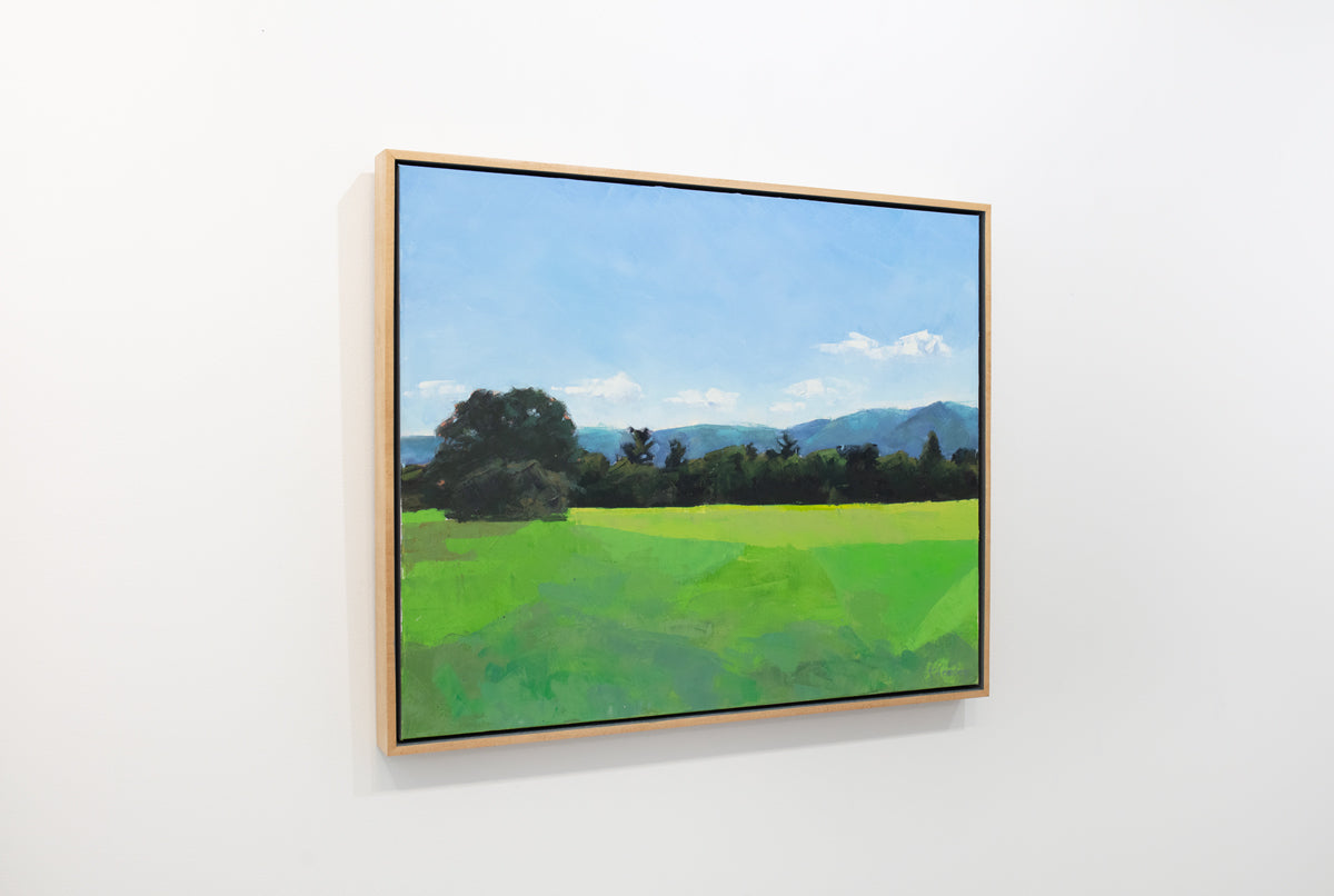 A blue and green landscape painting in a wood frame hangs on a white wall.