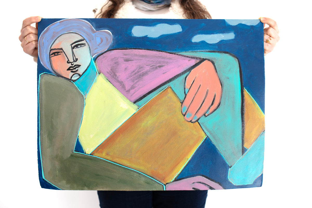 A woman holds a colorful painting of a woman on paper in front of a white wall. 