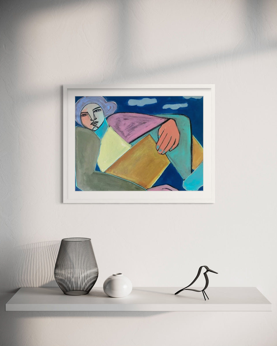 A colorful painting of a geometric, abstracted woman framed in a white frame hangs on a white wall above a white floating shelf with black and white table decor. 
