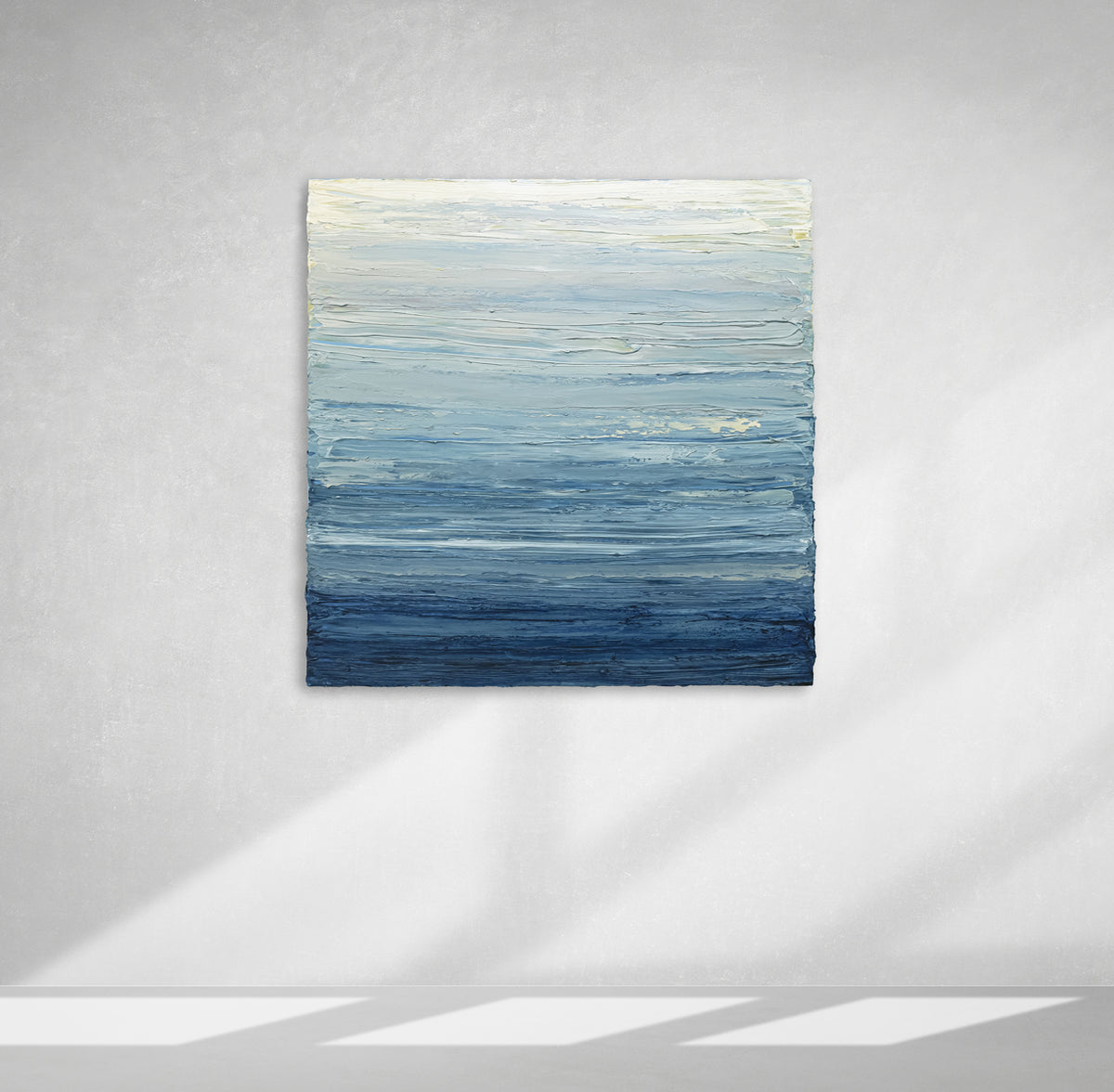 A blue, beige, lavender and light yellow textured abstract painting by Teodora Guererra hangs on a wall.