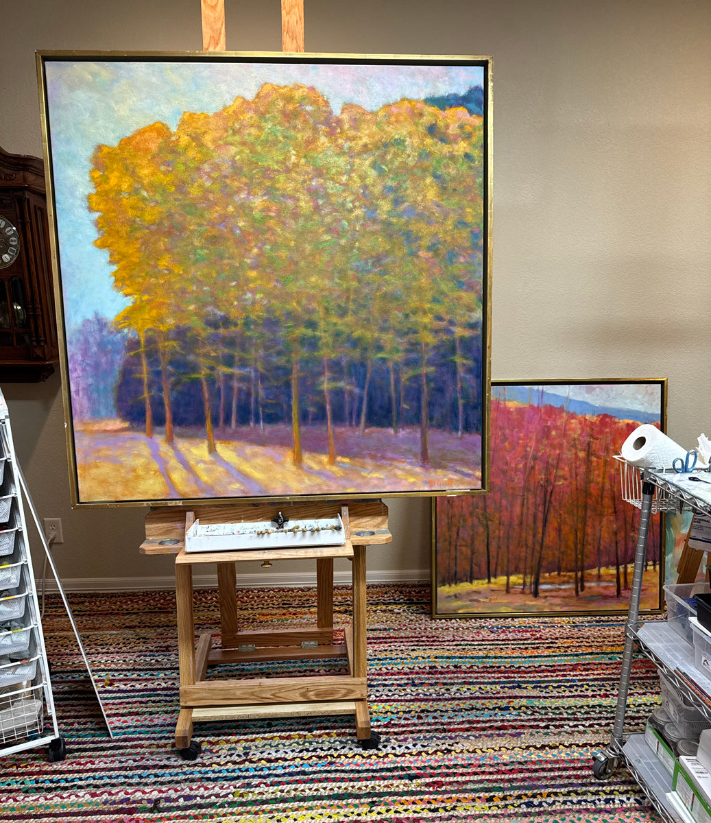 Painting of trees in autumn colors on an easel in a studio setting.