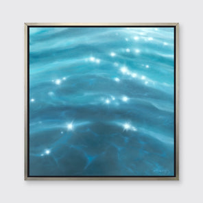 A tonal blue and white seascape print in a silver floater frame hangs on a white wall.