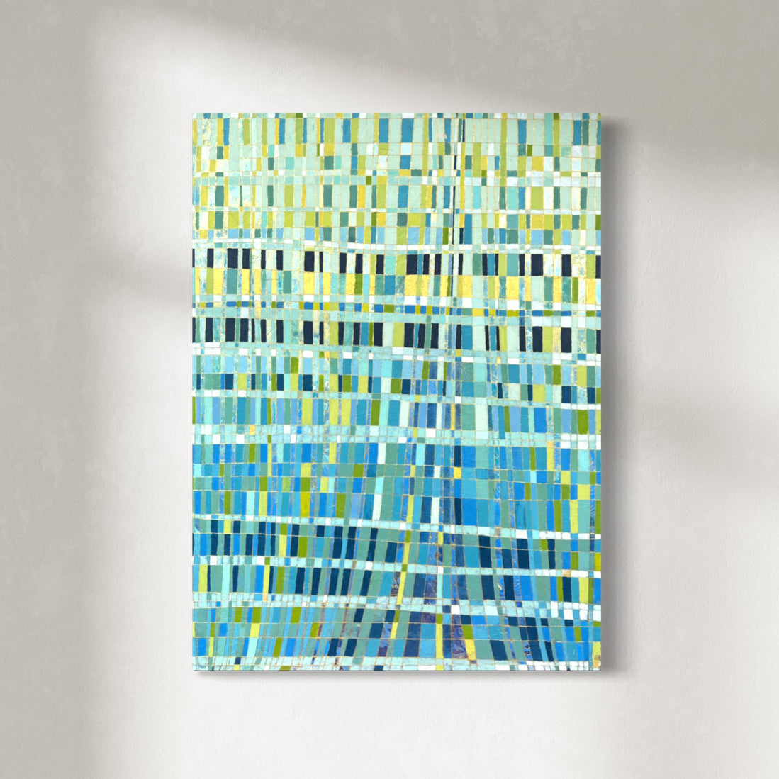 An abstract painting with a mosaic of blue, teal, green, and yellow vertical rectangular blocks, hanging on a light gray textured wall.