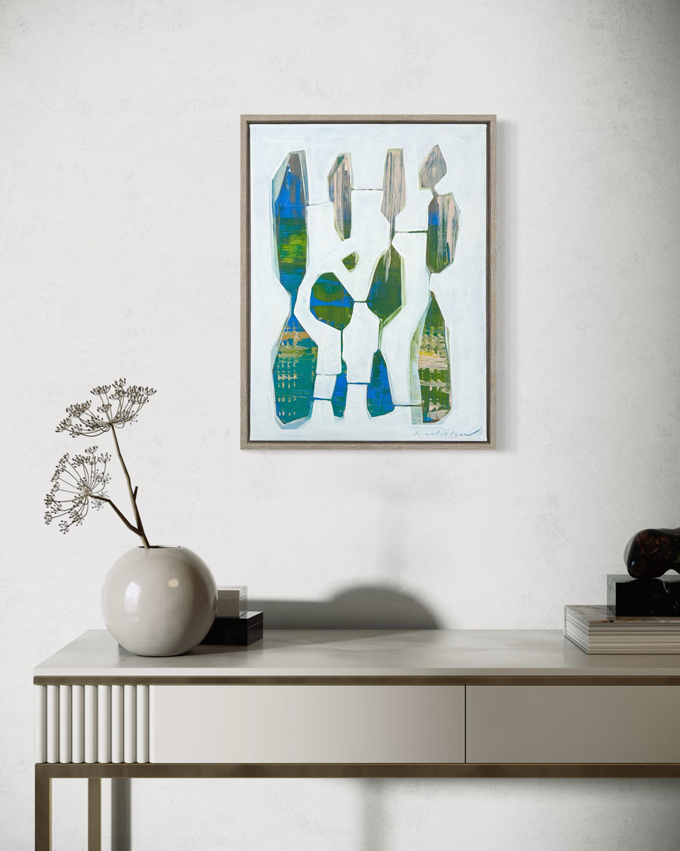 A framed abstract painting hangs on a white wall above a modern console table with modern table decor. 