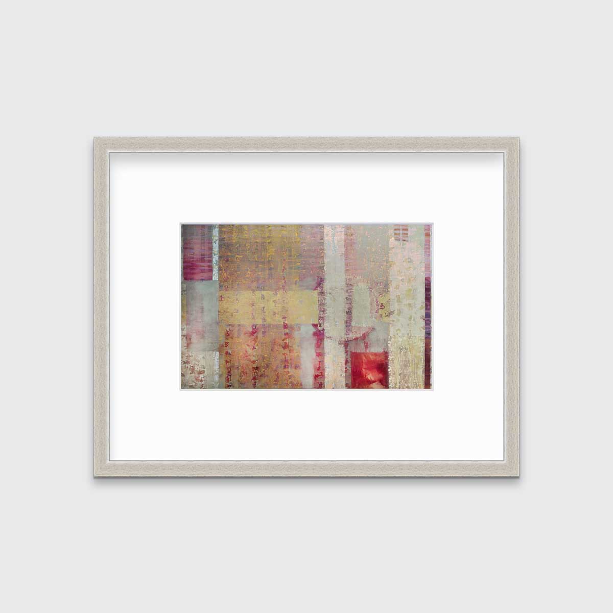 A red, yellow and grey abstract print in a silver frame with a mat hangs on a white wall.
