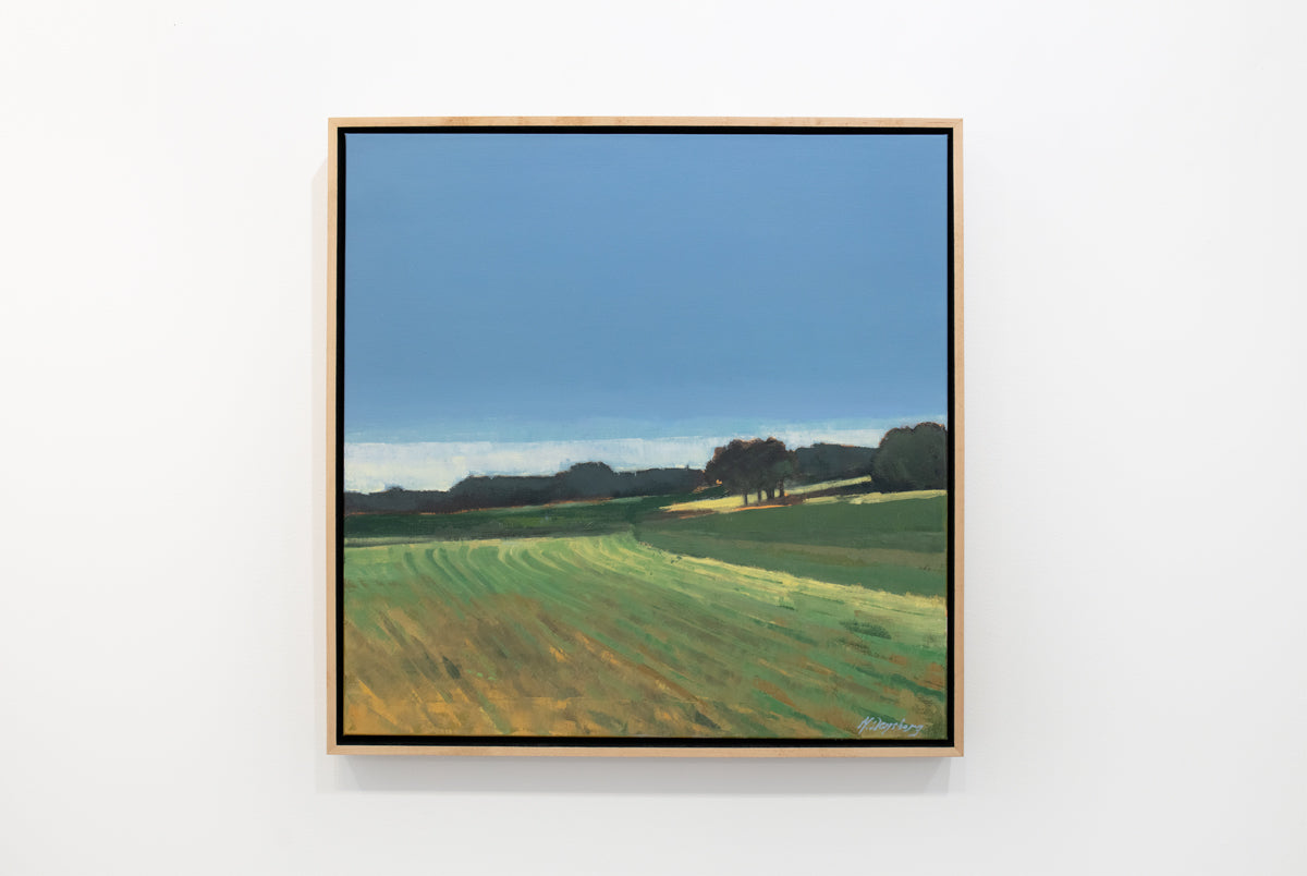 A green and blue abstracted landscape painting in a light wood frame hangs on a white wall. 