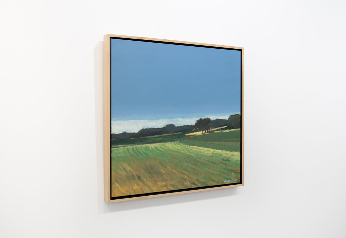 A green and blue abstracted landscape painting in a light wood frame hangs on a white wall.
