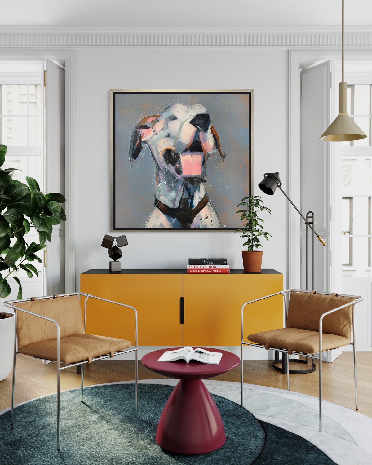 A white, light pink, grey and brown abstract dog print in a silver floater frame hangs on a white wall above a yellow and black credenza with decorative accessories, two low chrome and tan cushioned chairs and a small raspberry pedestal side table.